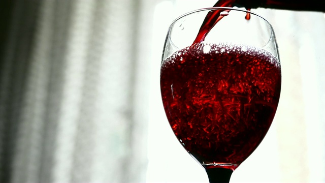 在灯光背景下，红酒倒入玻璃杯中视频素材