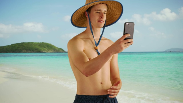 迷人的年轻单身汉在海滩上使用智能手机的肖像。白人男性在加勒比海海岸用手机发短信。4 k视频素材
