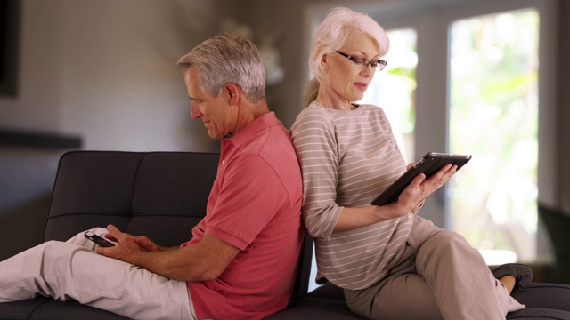 一对老年夫妇在家里的沙发上使用电子设备视频下载