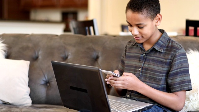非洲裔少年在家里使用手机，笔记本电脑。视频下载