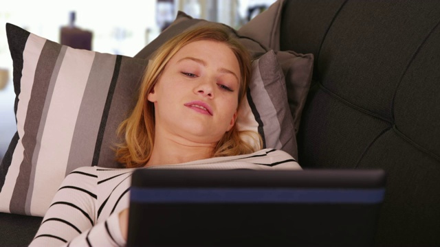 年轻的白人妇女躺在沙发上使用笔记本电脑的特写视频素材