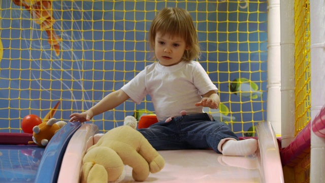 在游戏中心，可爱的小女孩从毛绒玩具的滑梯上滚下来视频下载