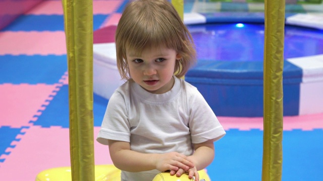 可爱的小女孩在儿童娱乐中心的旋转木马上微笑着旋转视频下载