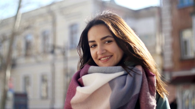 可爱的女孩穿着华丽的围巾和夹克在街道上微笑在冬天的慢镜头视频下载