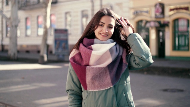在慢镜头中，穿着条纹围巾和夹克衫的快乐女孩在冬天的街道上微笑视频下载
