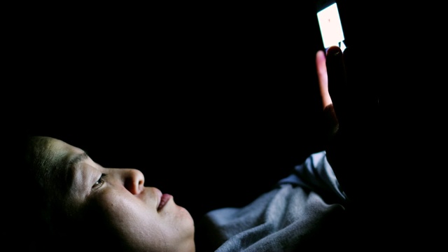 亚洲妇女躺在床上，使用手机在黑暗的夜晚视频下载