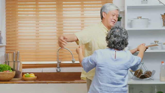 快乐的亚洲老年夫妇在厨房跳舞在家，退休生活方式，积极的老年概念视频素材