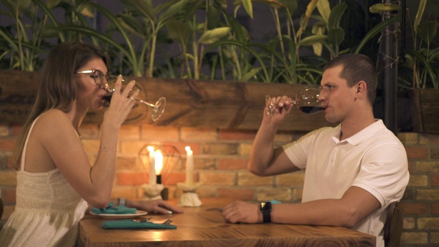 幸福的情侣在餐厅享用烛光晚餐时喝红酒。男男女女在餐厅浪漫约会时喝着酒杯里的红酒视频下载