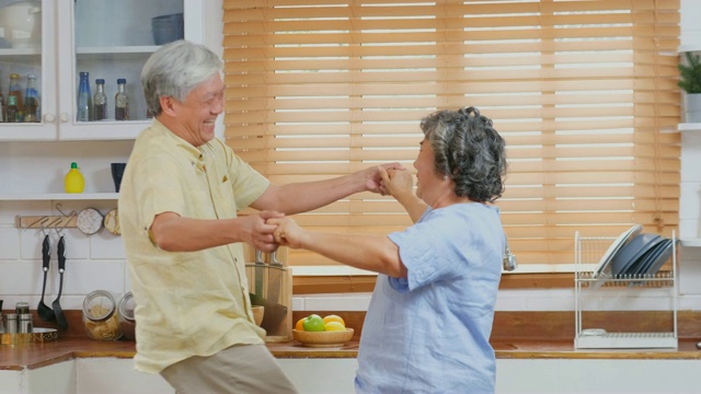 快乐的亚洲老年夫妇在厨房跳舞在家，退休生活方式，积极的老年概念视频素材