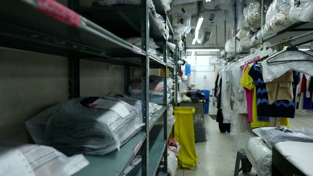 拉丁美洲男性雇员在工业洗衣服务寻找一件装在架子上的袋子里的衣服视频素材