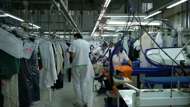 拉丁美洲雇员在一个工业洗衣服务熨烫和晾衣服视频下载