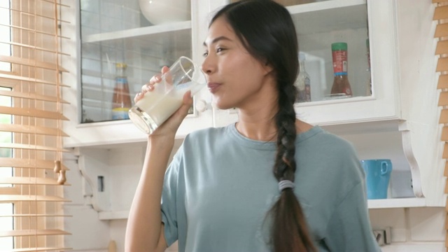 年轻美丽的亚洲女人喝着牛奶，在厨房跳舞，快乐健康的生活方式视频素材