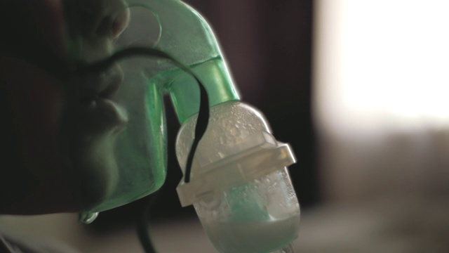 一个小男孩通过呼吸器的透明面罩呼吸。孩子吸进了吸入器。给病人戴上吸入面罩视频素材