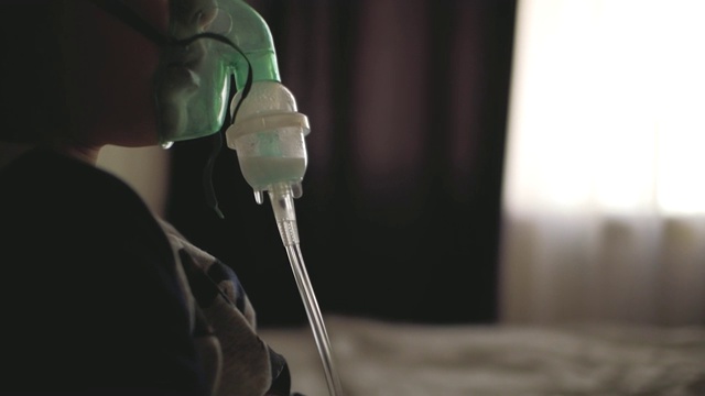 一个男孩通过呼吸器的透明面罩呼吸。孩子吸进了吸入器。给病人戴上吸入面罩视频素材
