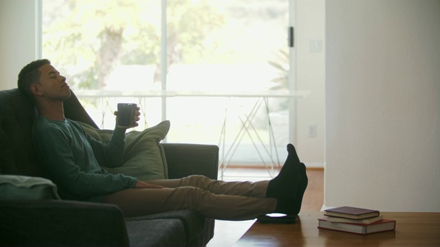 年轻男子喝着咖啡，在家里放松视频下载