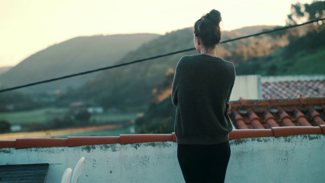 女人在屋顶阳台上喝水，在早晨看风景视频素材