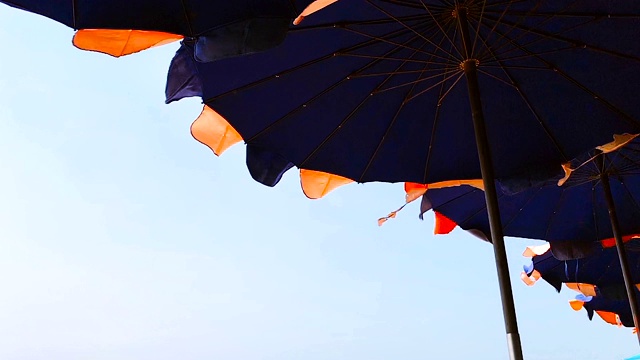慢动作拍摄风吹着沙滩床上的遮阳伞，蓝天为背景。视频素材