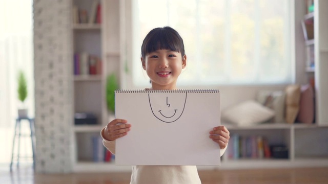 女孩面带微笑，拿着画纸，脸上洋溢着幸福的神情视频下载