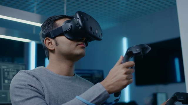 软件开发者戴着虚拟现实耳机手势与控制器开发和程序VR游戏和应用。在计算机和显示器的后台技术开发工作室视频下载