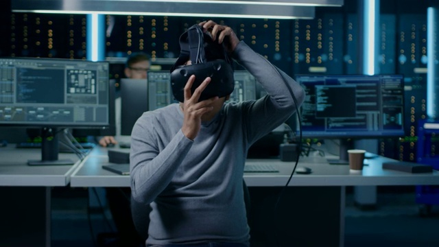 肖像的软件开发人员戴上虚拟现实耳机持有控制器和开始编程在VR。在计算机和显示器的后台技术开发工作室视频素材