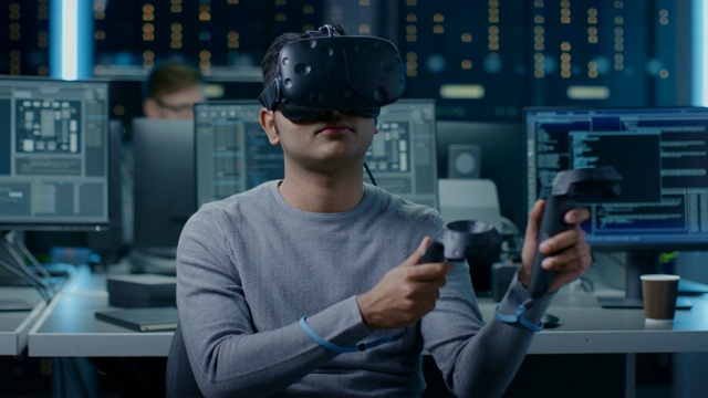 软件开发者戴着虚拟现实耳机手势与控制器开发和程序VR游戏和应用。在计算机和显示器的后台技术开发工作室视频素材