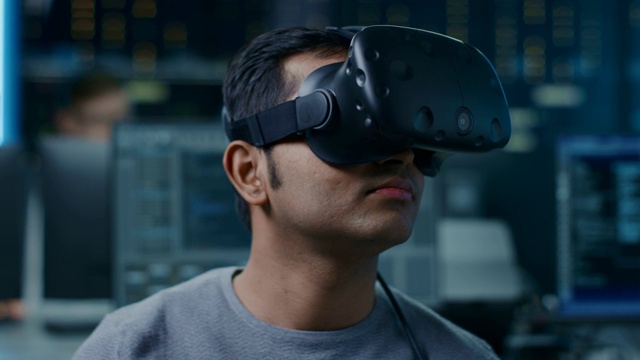 软件开发者戴着虚拟现实头盔，用他的头做手势，开发和编程虚拟现实游戏或应用程序。在计算机和显示器的后台技术开发工作室视频素材