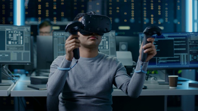 软件开发者戴着虚拟现实耳机手势与控制器开发和程序VR游戏和应用。在计算机和显示器的后台技术开发工作室视频素材