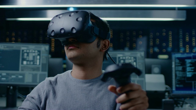软件开发者戴着虚拟现实耳机使用控制器开发和程序VR游戏和应用程序。在计算机和显示器的后台技术开发工作室视频素材
