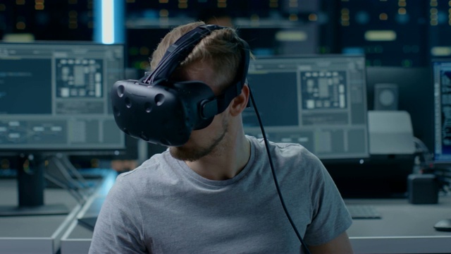 软件开发者戴着虚拟现实头盔，用他的头做手势，开发和编程虚拟现实游戏或应用程序。在计算机和显示器的后台技术开发工作室视频素材