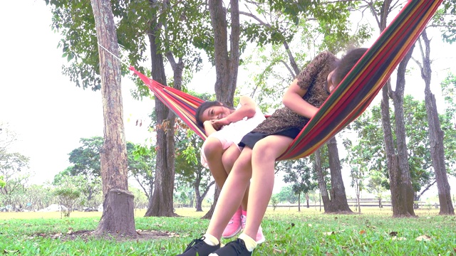两个年轻女子在树下的吊床上荡秋千视频素材