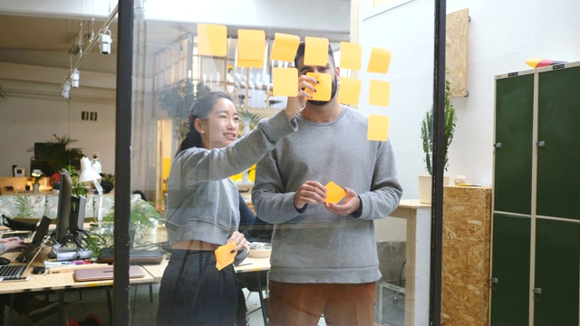 手持拍摄的年轻的商业同事讨论在玻璃墙上的粘合剂在新办公室视频素材