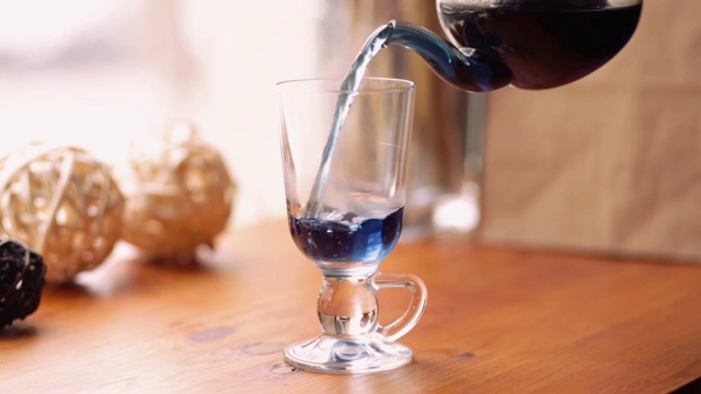 蓝蝴蝶豌豆茶，从花阴蒂里亚在咖啡馆的桌上。泰国花蓝色茶倒入一个透明的杯子。茶减肥，健康，排毒视频素材