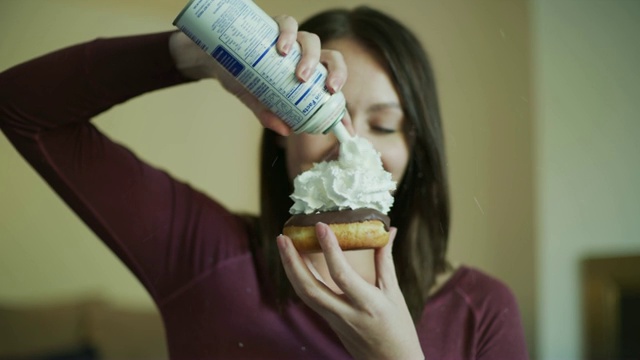美国犹他州默里，一位微笑的女士在巧克力甜甜圈上喷洒鲜奶油，然后开始吃视频下载