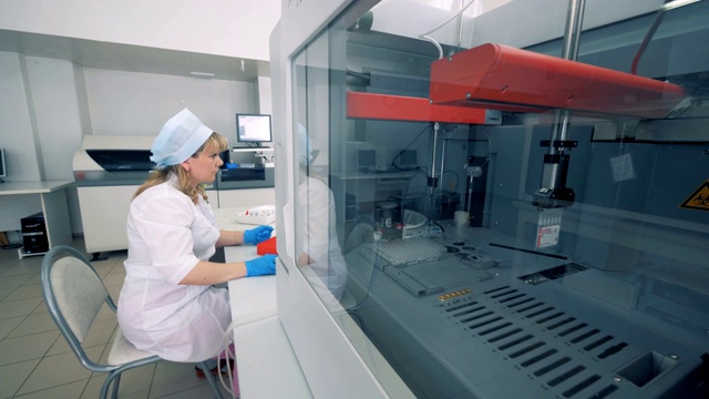 生化分析仪正在检测样品，一名女工在控制过程视频素材