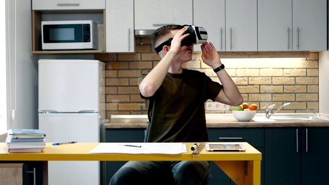 年轻人戴上虚拟现实眼镜，坐在厨房里工作。视频下载