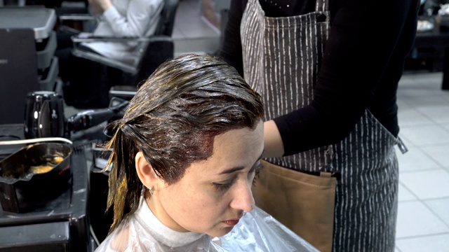 在理发店染发。一个成年女孩坐在理发店里，理发师正在给她涂头发。头发护理。关闭了。4 k。25 fps。视频下载
