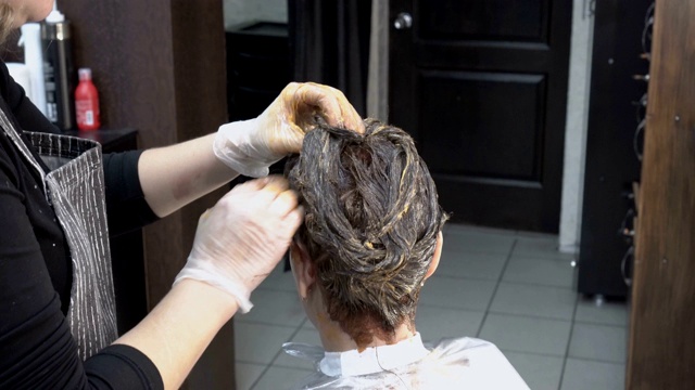 在美容院里，一位专业的美发师正在往女孩的头发上涂抹颜料。在发廊染发的程序。头发护理。关闭了。4 k。25 fps。视频下载