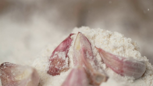慢镜头:白面粉撒在未剥皮的蒜瓣上。视频素材