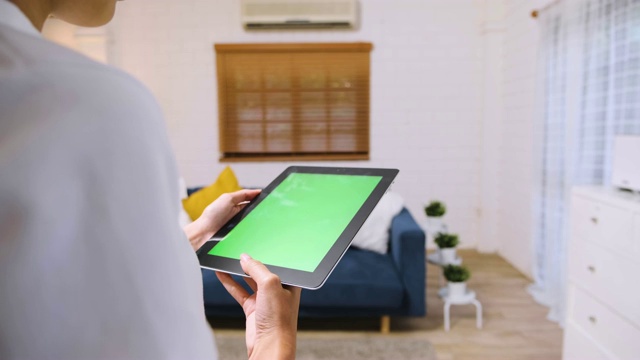 女人用绿屏平板电脑应用来控制家里客厅的空调。智能家居自动化控制概念。视频素材