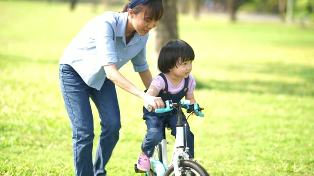 亚洲小女孩和年轻的老师在花园里骑自行车视频素材