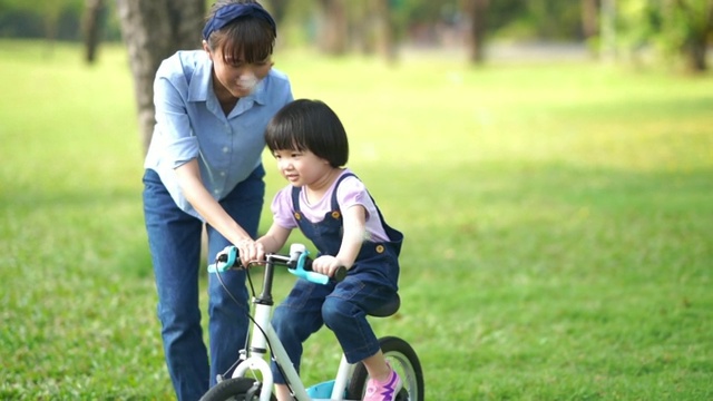 亚洲小女孩和年轻的老师在花园里骑自行车视频素材