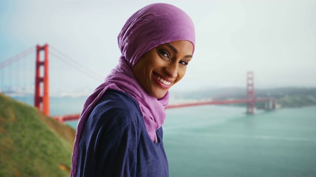 迷人的黑人妇女戴着头巾参观金门大桥，对着镜头微笑视频下载