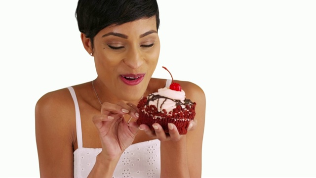 黑色女性在工作室微笑着吃着红色天鹅绒纸杯蛋糕的特写视频素材