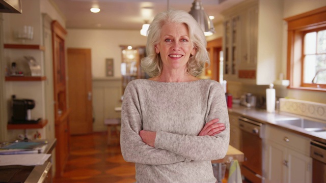 在迷人的厨房里，穿着灰色毛衣的开朗的老妇人对着镜头微笑视频素材