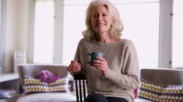 快乐的老妇人拿着咖啡杯在家里打响指微笑视频素材