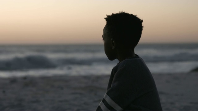 一个沉思的男孩在夕阳下看着大海视频下载