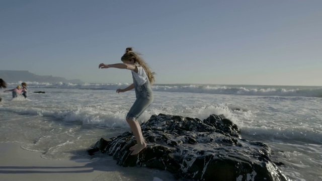 在海滩上，女孩在岩石上躲避海浪视频素材