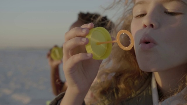 女孩和男孩吹泡泡的特写在有风的一天在海滩上视频素材