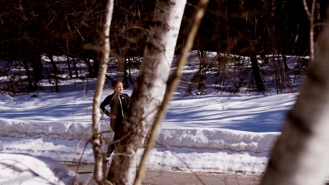 在阳光明媚的冬日里，年轻的女运动员在一条山路上跑步。——股票视频视频素材