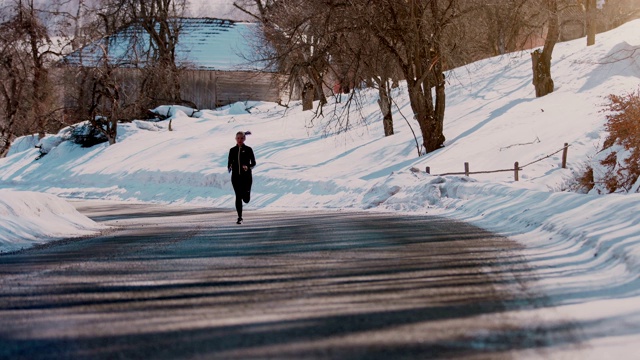 在阳光明媚的冬日里，年轻的女运动员在一条山路上跑步。——股票视频视频素材